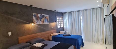 A hotel room with two beds, a painting on the wall, a window with curtains, and a ceiling fan.