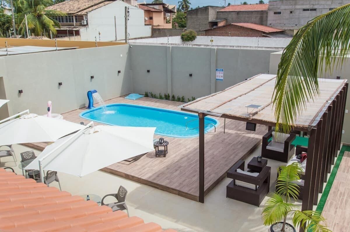 Una piscina en la azotea con terraza de madera, sombrillas blancas y mobiliario de exterior.