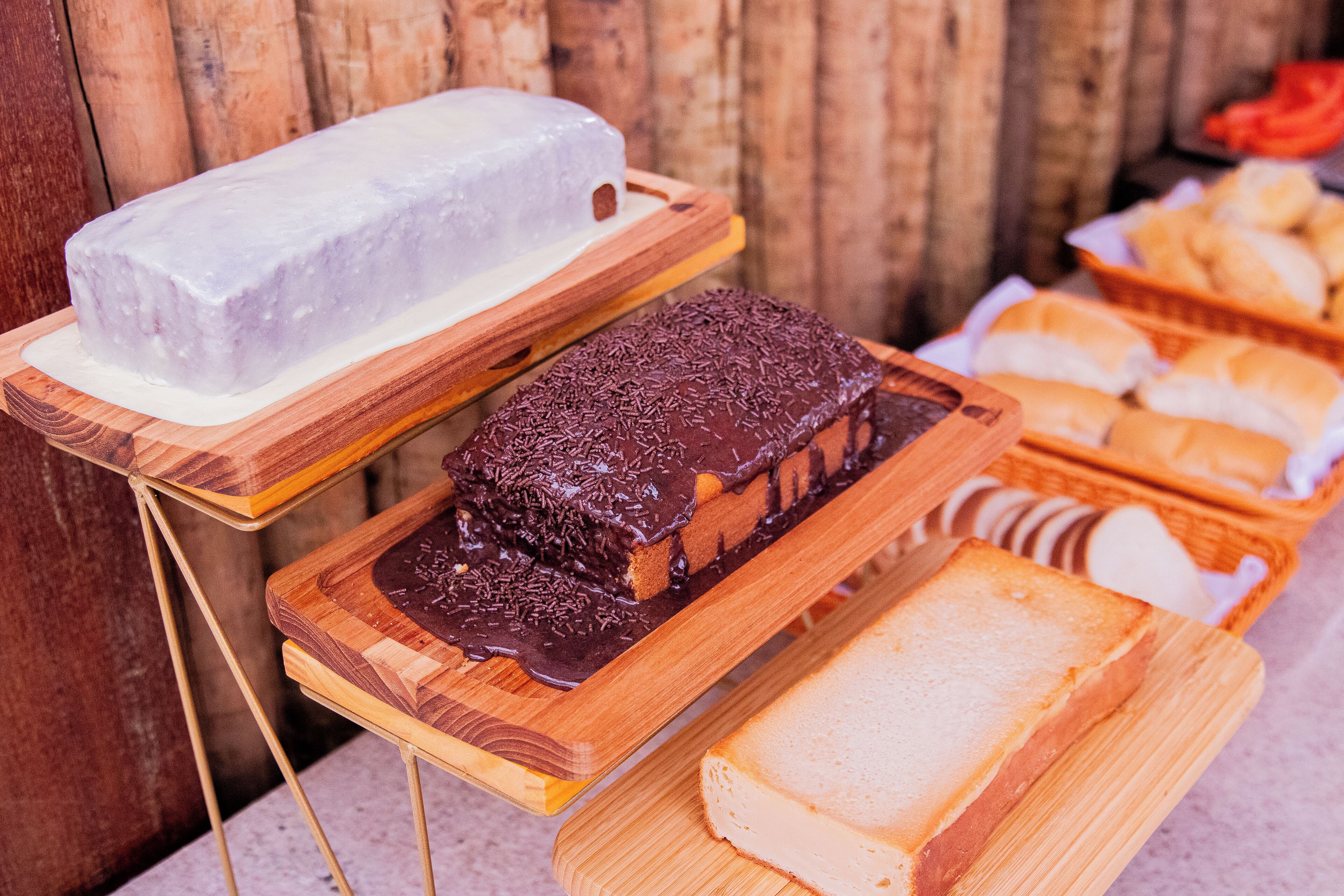 A display of desserts on wooden boards, including a white cake, a chocolate-covered cake, and several slices of bread.