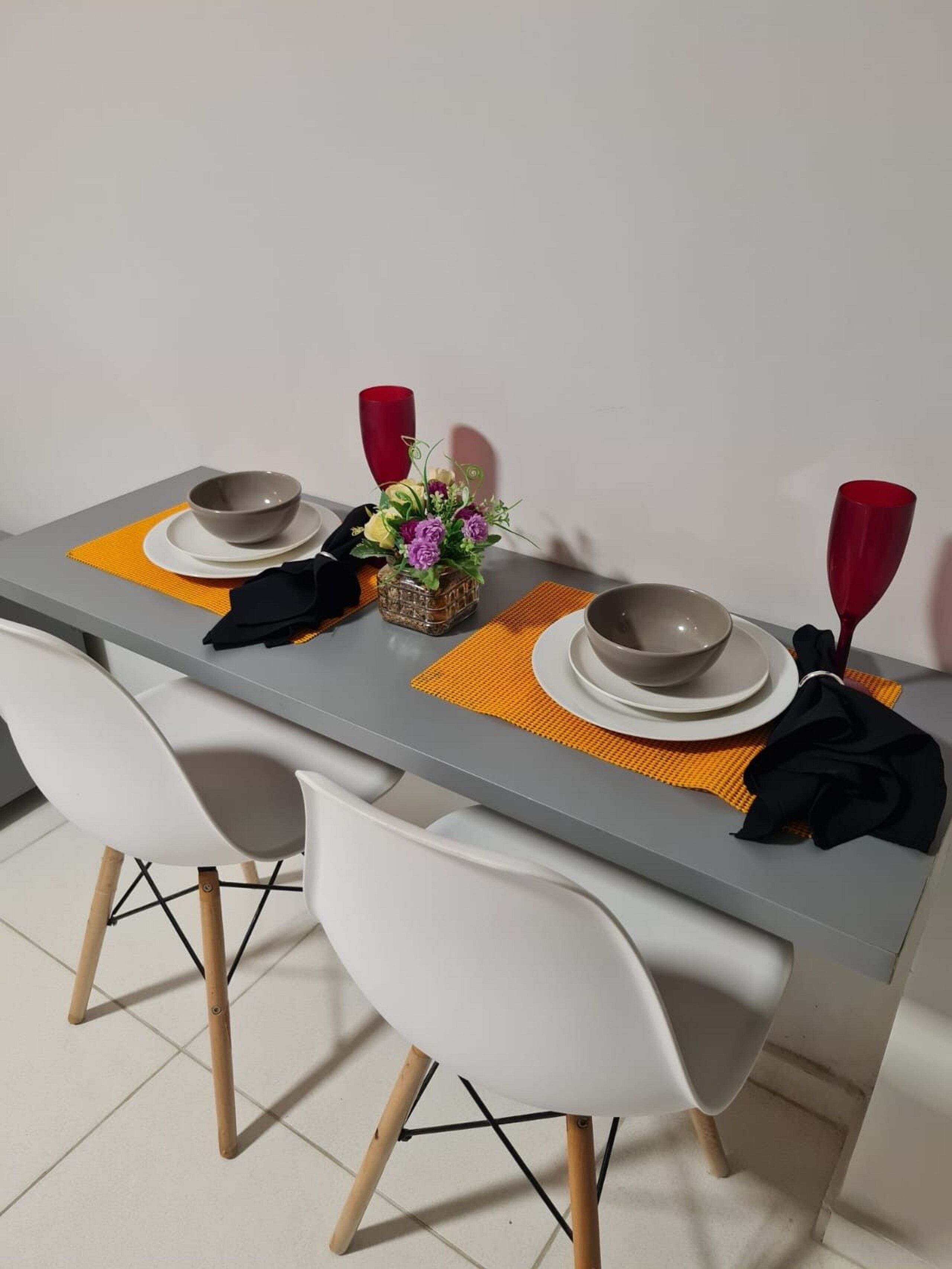 Una mesa de comedor con dos sillas blancas, mantel gris y cristalería roja.