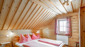 Ein Schlafzimmer einer Holzhütte mit geneigter Decke, einem Bett mit roten Karomustern, einem Fenster mit Karovorhängen und einem Heizkörper.
