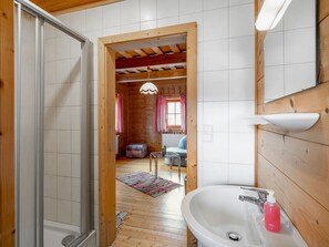 Ett interiört utrymme med träinredning och ett badrum som har ett handfat, en dusch och ett fönster med gardiner.