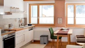 A modern kitchen with a stove, sink, and wooden countertop. There is a dining area with a table and chairs, and a window with blinds. - Apartment Falch by Interhome (Flirsch)
