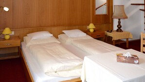 A hotel room with two single beds, wooden headboard, bedside lamps, a small table with a lamp, and a chair. - Apartment Falch by Interhome (Flirsch)