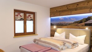 Ein Schlafzimmer mit Bett, einem Fenster mit Jalousien, einem Holz-Kopfstück und einer Wandlampe.