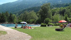 Een zwembad met mensen die zonnebaden en zwemmen, omringd door weelderige begroeiing en bergen op de achtergrond.