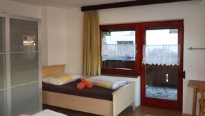 Een slaapkamer met twee bedden, een raam met gordijnen, een deur naar een balkon en een klein tafeltje.