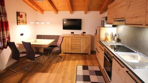 A compact kitchen with wooden cabinets, a built-in oven, a sink, and a dining area with chairs and a table. - Piz Munschuns by Interhome (Spiss-Samnaun)