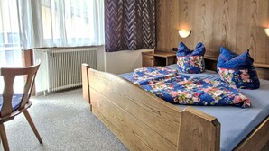 En seng med træstel, blomstret sengetøj, en stol, et skrivebord og en vægmonteret lampe.