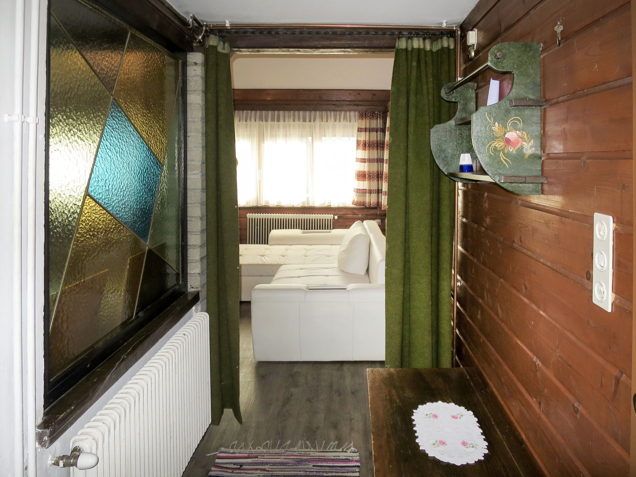 Un couloir étroit avec un radiateur, un canapé blanc et un mur en bois.