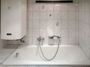 Een badkamer met een witte badkuip, een douchekop en een handdoekrek.