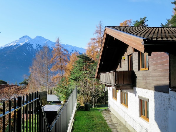 Een chalet met een houten balkon, een pad van stenen en uitzicht op besneeuwde bergen.