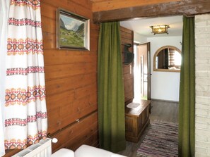 Een gezellige kamer met houten wanden, een lijst met een schilderij, een radiator, een houten bankje en een groen gordijn.
