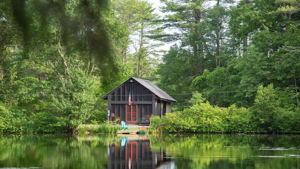 A cabin with a red door, surrounded by dense forest and a calm lake. - Catskills Cabin on 100 Wooded Acres with Lake (Climax)