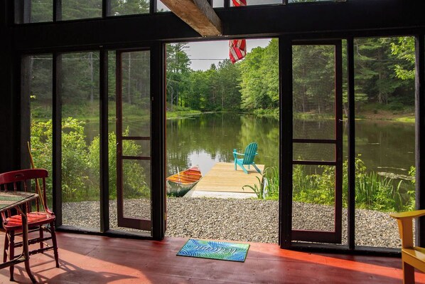Ein Zimmer mit großen Fenstern mit Blick auf einen See, eine Anlegestelle mit einem Boot und Sitzgelegenheiten im Freien.