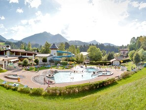 A resort with multiple swimming pools, a water slide, and a mountain backdrop.