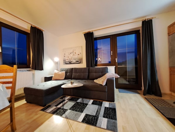 A modern living room with a sectional sofa, a small coffee table, and a view of the outdoors through large windows.