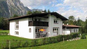 A two-story white house with a balcony, a dining area with outdoor seating, and a mountain backdrop. - Vacation home Anger by Interhome (Angerberg)
