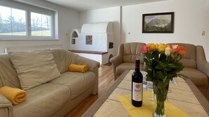 A living room with a beige sofa, a yellow throw pillow, a table with a bottle of Servos wine, and a vase with flowers. - Vacation home Anger by Interhome (Angerberg)