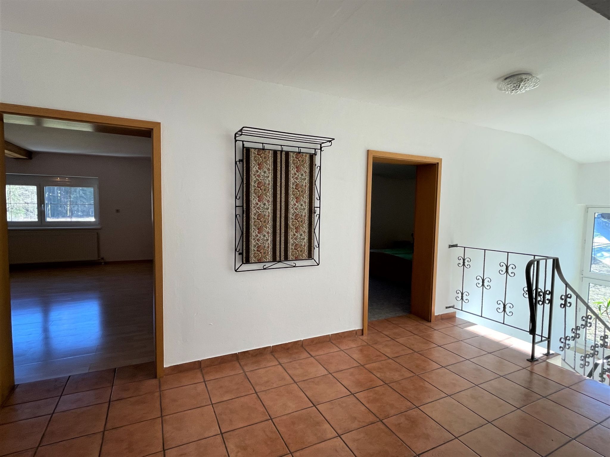 Um quarto amplo com piso de azulejos, uma janela com moldura decorativa e uma escadaria com corrimão de metal.