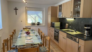 A modern kitchen with wooden cabinets, a dining table with chairs, and a cross on the wall. - Vacation home Anger by Interhome (Angerberg)