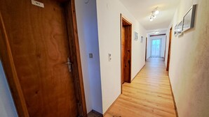 Un pasillo con suelo de madera y puertas, una de ellas con la etiqueta 'WE'.