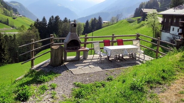 A rustic outdoor seating area with a stone oven, wooden fence, and a table with chairs. - Oberhaus by Interhome (Finkenberg)