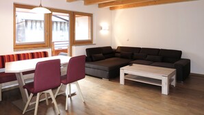Una sala de estar moderna con techo de madera, un sofá seccional, una mesa de comedor con sillas y ventanas grandes.