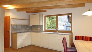 Una cocina con armarios blancos, encimera de granito y ventana con vista a follaje.