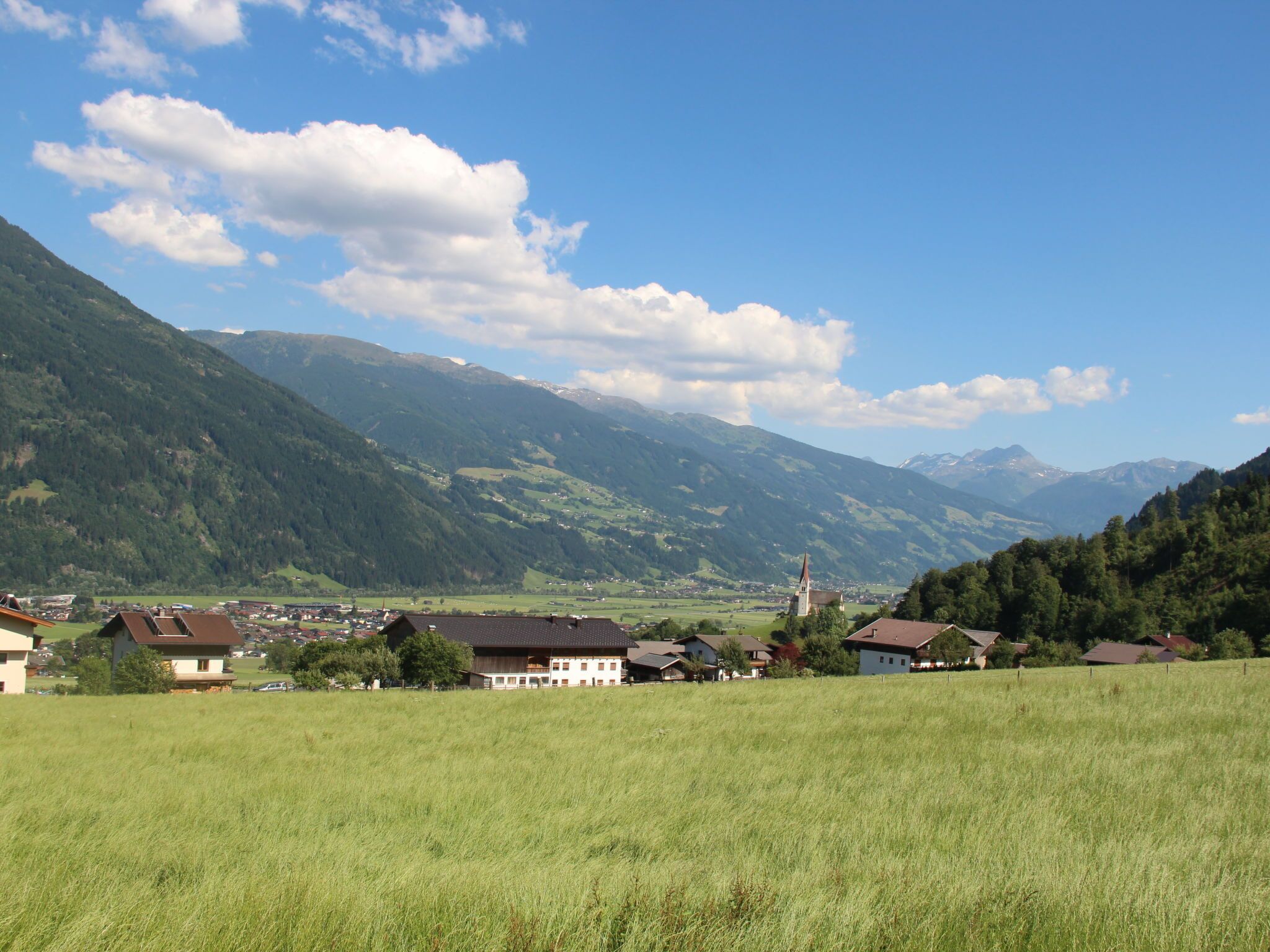 Ein ländliches Dorf mit Häusern und einer Kirche, umgeben von Bergen und blauem Himmel.