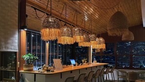 Un espace bar avec un plafond en bois, des luminaires en fibres tressées et une vue sur la ville grâce à de grandes fenêtres.