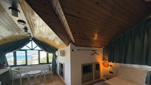 Une pièce confortable avec un lit, une table entourée de chaises, une cheminée et une vue sur la mer.