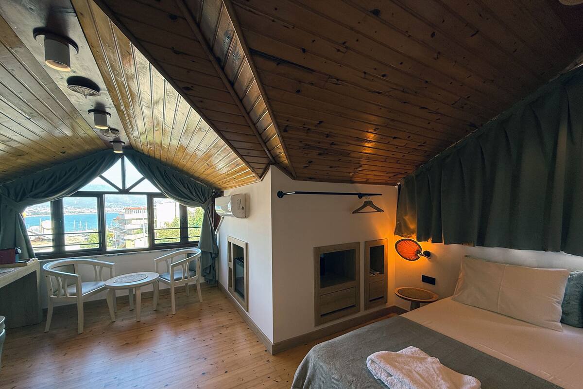 Une pièce confortable avec un lit, une table entourée de chaises, une cheminée et une vue sur la mer.