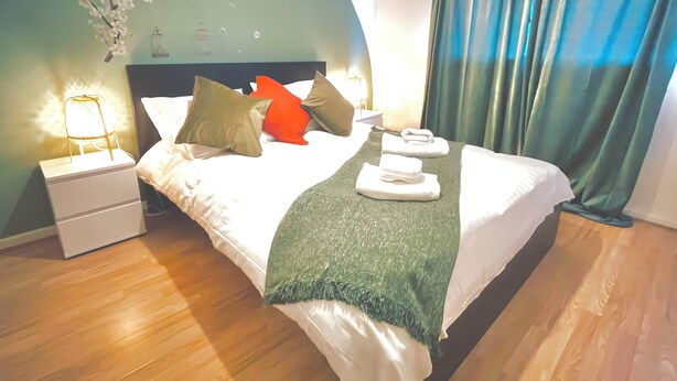 Uma cama bem arrumada com almofadas, uma luminária de cabeceira e um cobertor verde.