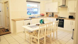 Uma cozinha moderna com armários brancos, uma mesa de jantar com cadeiras, uma janela e um forno embutido.