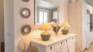Een witte console tafel met twee lampen, een spiegel erboven en decoratieve borden aan de muur.