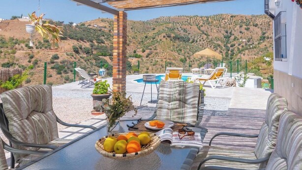 Een terras met buitenmeubilair, een tafel met fruit, een zwembad en uitzicht op heuvels.