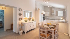 Een moderne keuken met witte kastjes, een eethoek met een houten tafel en stoelen, en een grote spiegel boven het aanrecht.
