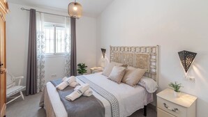 Een keurig opgemaakt slaapkamer met een bed, nachtkastjes, een stoel en een raam met gordijnen.