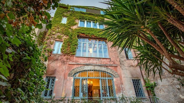 En bygning med en rosa facade, store vinduer og en balkon med plantekasser.