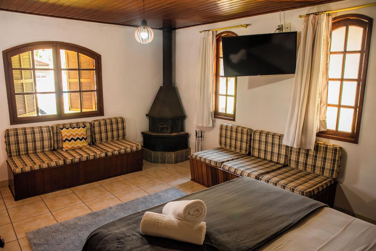 A cozy room with a fireplace, two plaid sofas, a bed, and a TV on the wall.