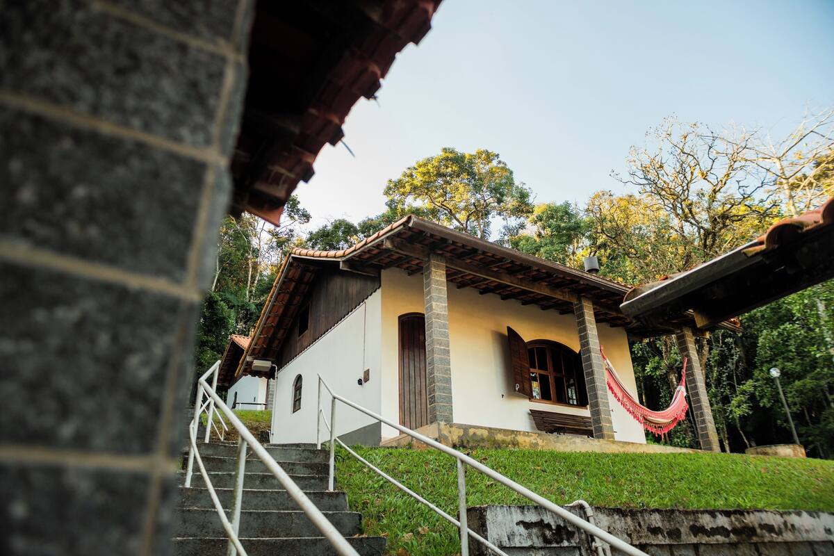 A house with a stone staircase leading to a wooden door, surrounded by greenery.