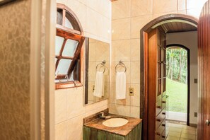 A bathroom with a marble sink, wooden vanity, and a window with a view of greenery. - Pousada Tapera (Itatiaia)