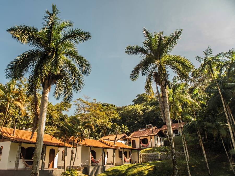 A colonial-style building with multiple rooms, palm trees, and a hilly landscape.