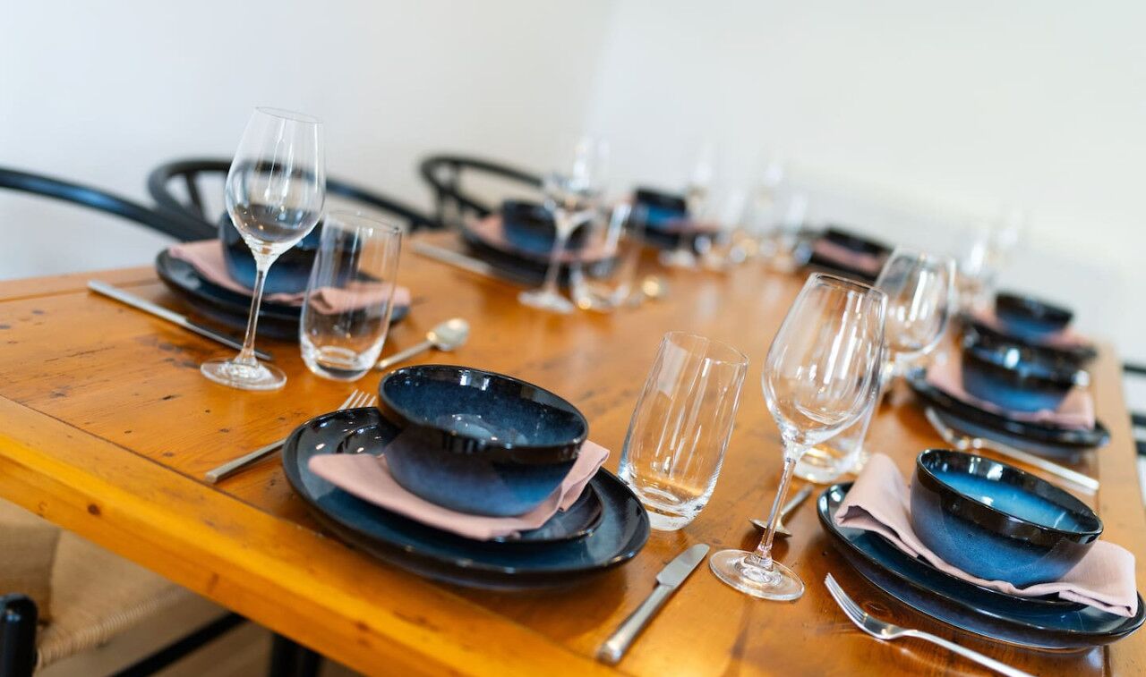 Una mesa de comedor dispuesta con varios platos, tazones y copas de vino, todo ordenado.