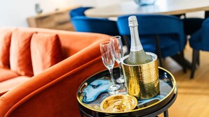 Eine Champagnerflasche auf einem Tablett mit zwei Gläsern, platziert auf einem Tisch in einem Raum mit einem roten Sofa und blauen Sesseln.