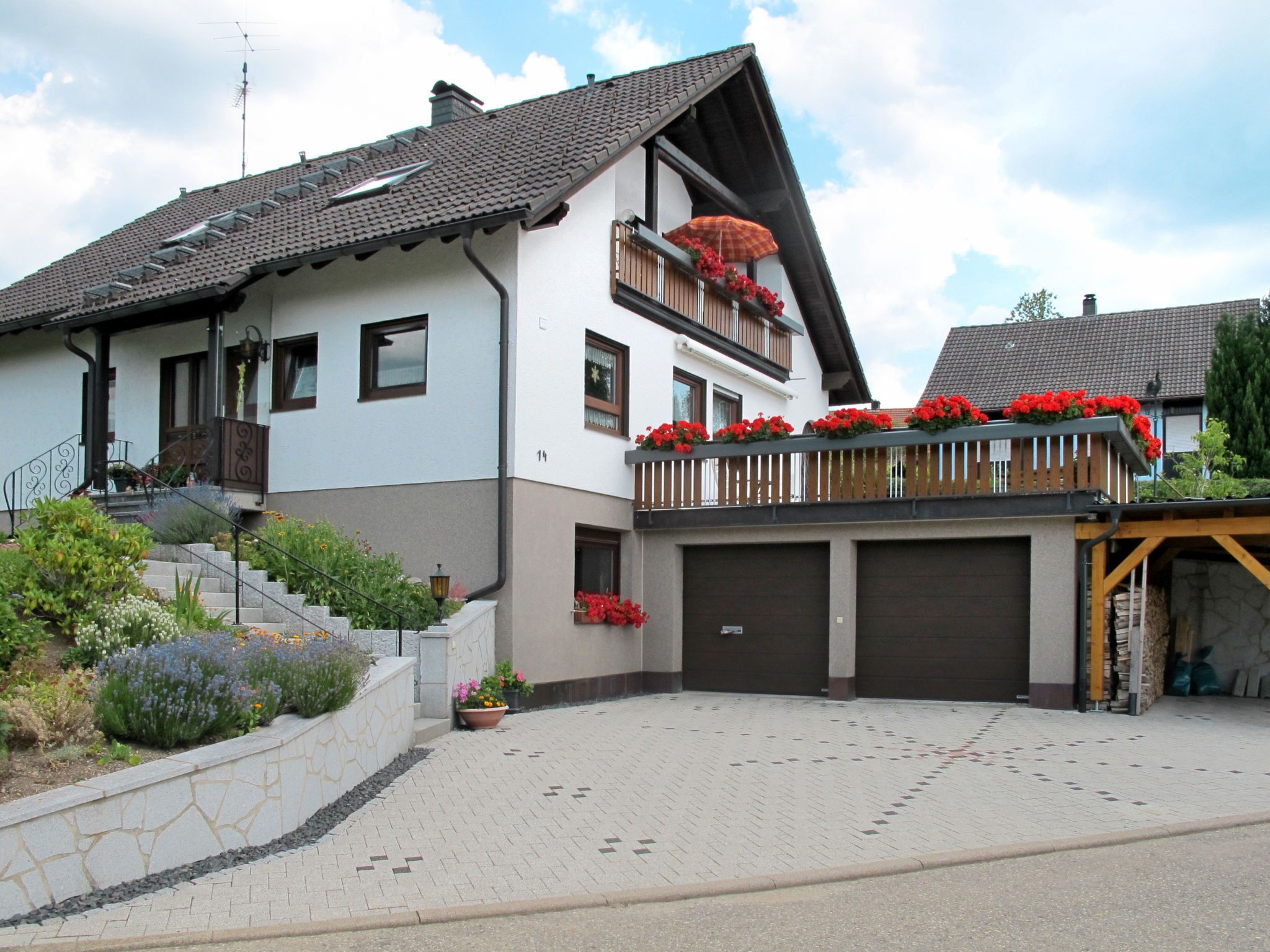 Een twee verdiepingen tellend huis met een balkon, een garage en een stenen steunmuur.