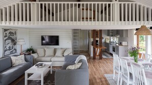 A spacious living room with a high ceiling, white railings, a flat-screen TV, and a cozy seating area with sofas and a coffee table.