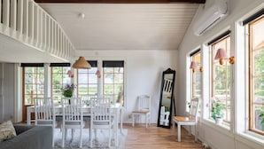 A spacious room with a dining area, a sofa, and large windows.