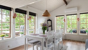 A dining area with white furniture, large windows, and a hanging light fixture.
